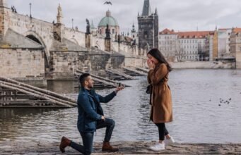 Where to Propose in Prague: 15 Best Spots and When to Go A man kneels to propose to a surprised woman on the Vltava embankment by Charles Bridge in Prague